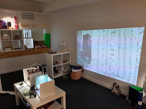 Das Bild zeigt, wie mit einer Webcam und einem Beamer das Gespielte live übertragen wird und auf eine weiße Wand projiziert wird